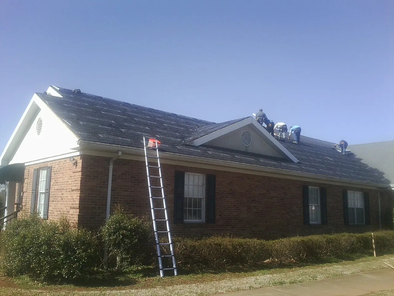 Crew tearing shingles off a brick ranch roof with a ladder set — Metal Roof Repair work by our crew in Seymour