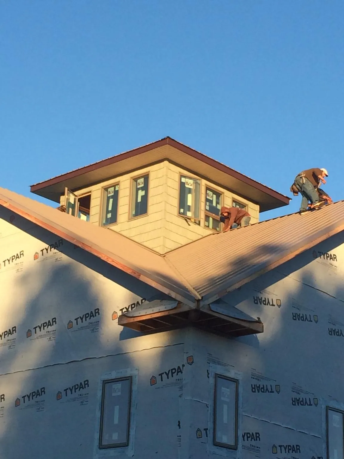 Roofers working around a rooftop cupola on a new metal roof at sunset in Seymour